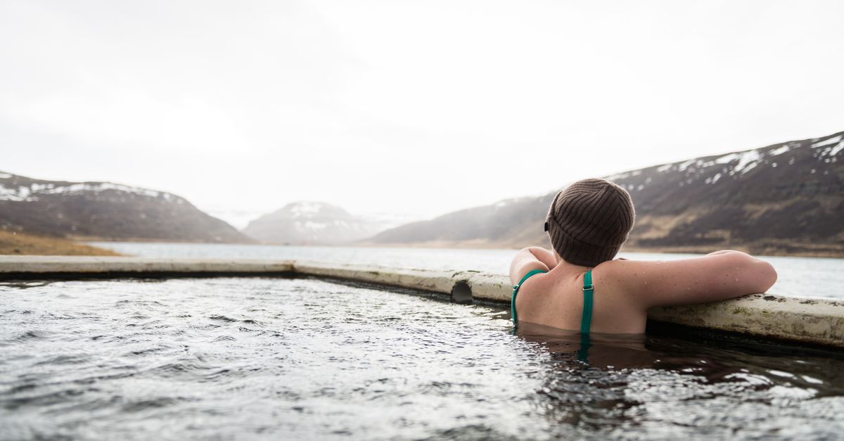 A person relaxes in a hot spring pool surrounded by snowy mountains and serene landscape.